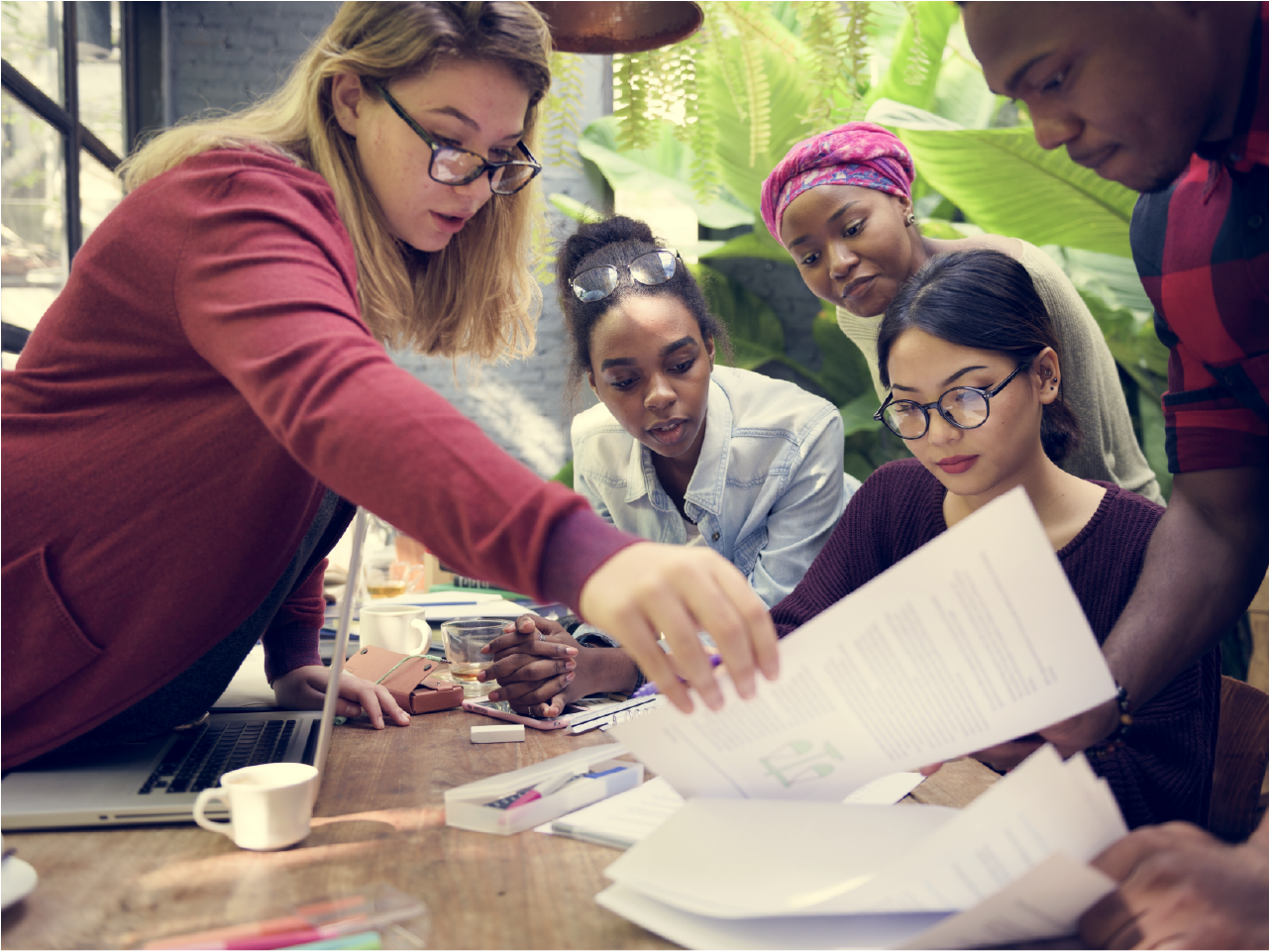 A diverse group of office workers collaborate on a report together at a desk.