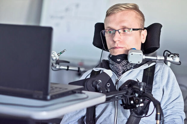 A man in a motorized wheelchair uses a microphone and head switch.