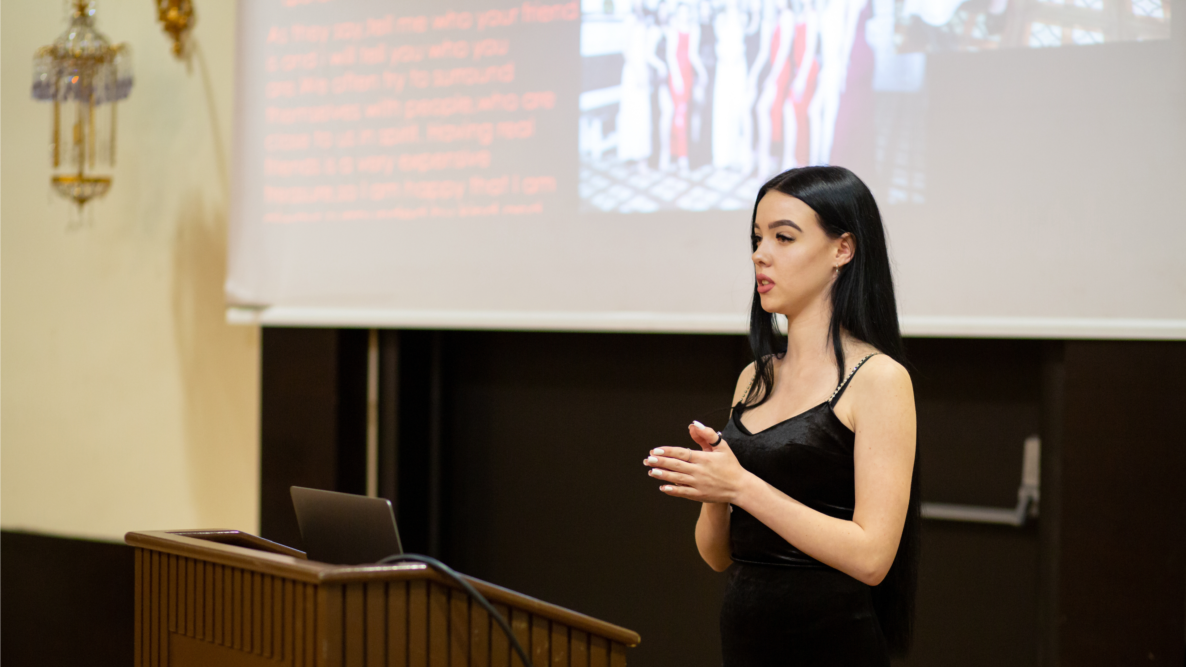 A woman presents at a podium with slides projected behind her.